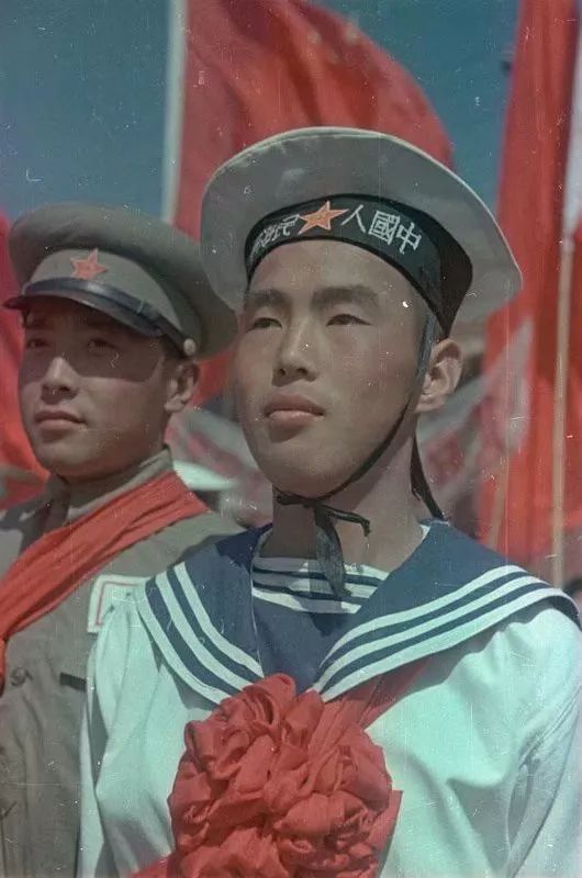 这是披红挂彩的海军战斗英雄，注意他的水兵服是非常早期的样式，八一帽徽在帽墙上，帽墙上从右至左书写“中国人民海军”，披肩上为三条白色线条。在之后的50式水兵服上，帽徽就移到帽檐上。现在的水兵帽上为从左至右的“中国人民解放军海军”，且更换成为简体字。披肩上的白色线条也增加为四条。